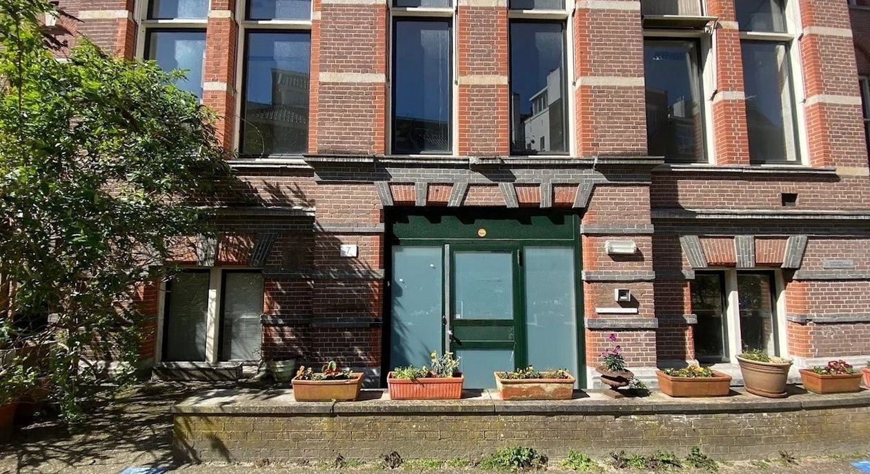 Het bakstenen gebouw met de groene voordeur en bloembakken