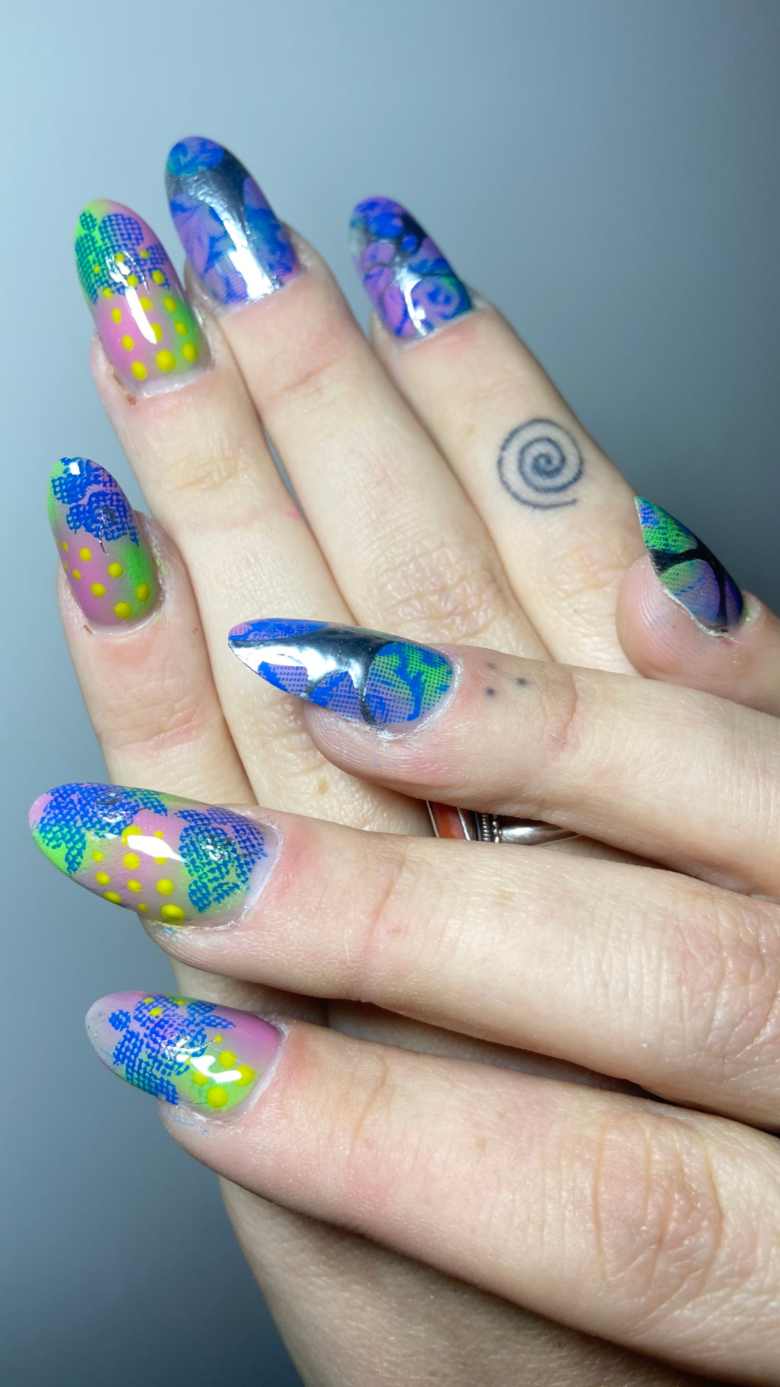 Lange amandelnagels vol blauwe, groene en gele nail art